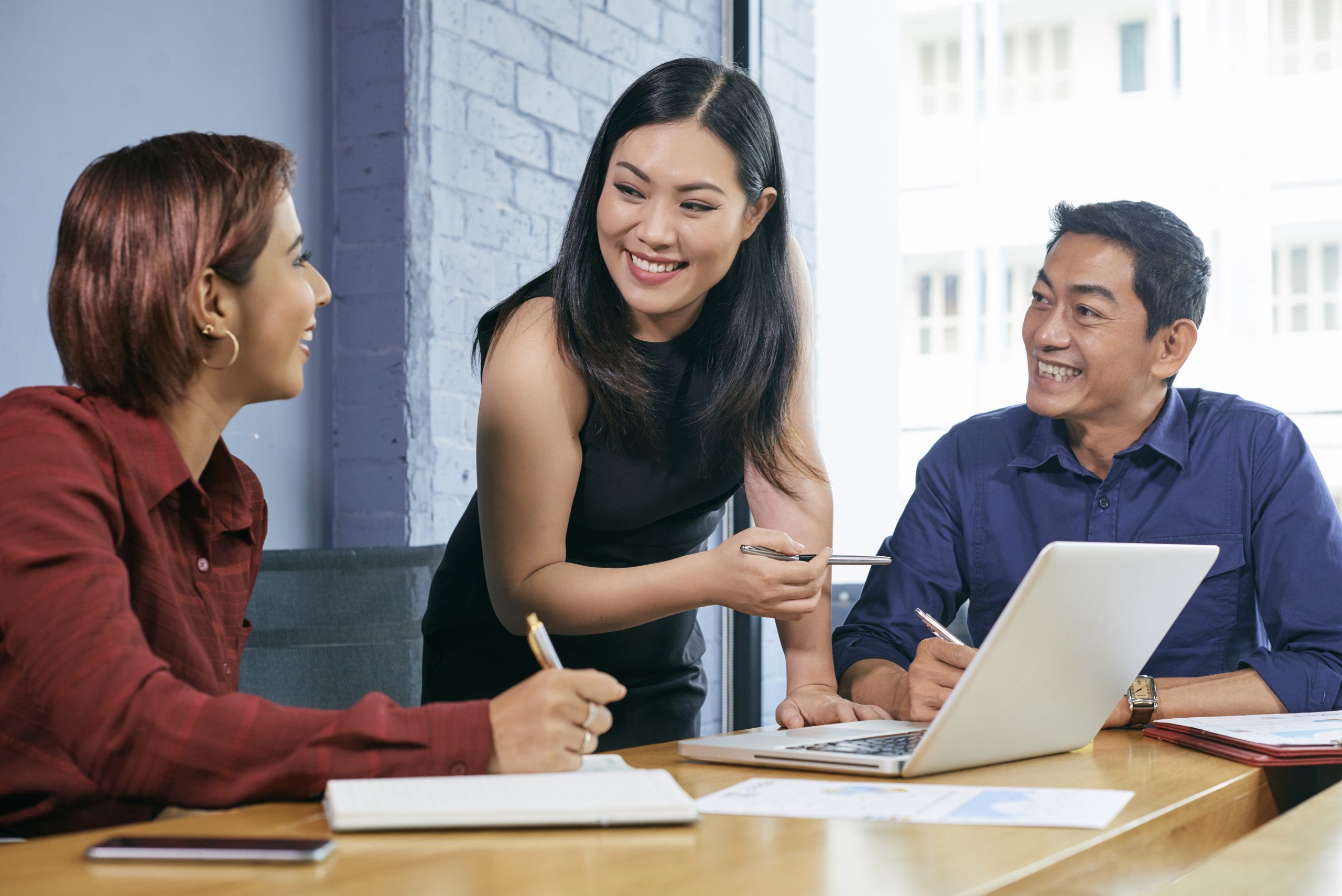 Smiling Vietnamese businesswoman discussing presentations on laptop screen with colleagues